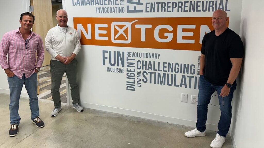 NextGen Culture – a word cloud that is in each of NextGen's offices, created by employees giving words to best describe the company's culture. Dwight Smith (chief financial officer), Frank Brewer (CEO) and Ryan Loughin (COO) are all pictured from left to right.